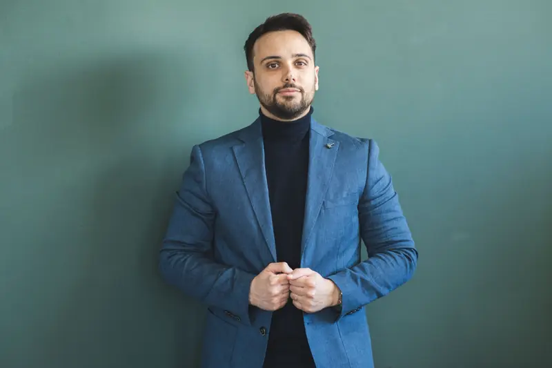 Luca Sacco in giacca blu davanti a una parete verde